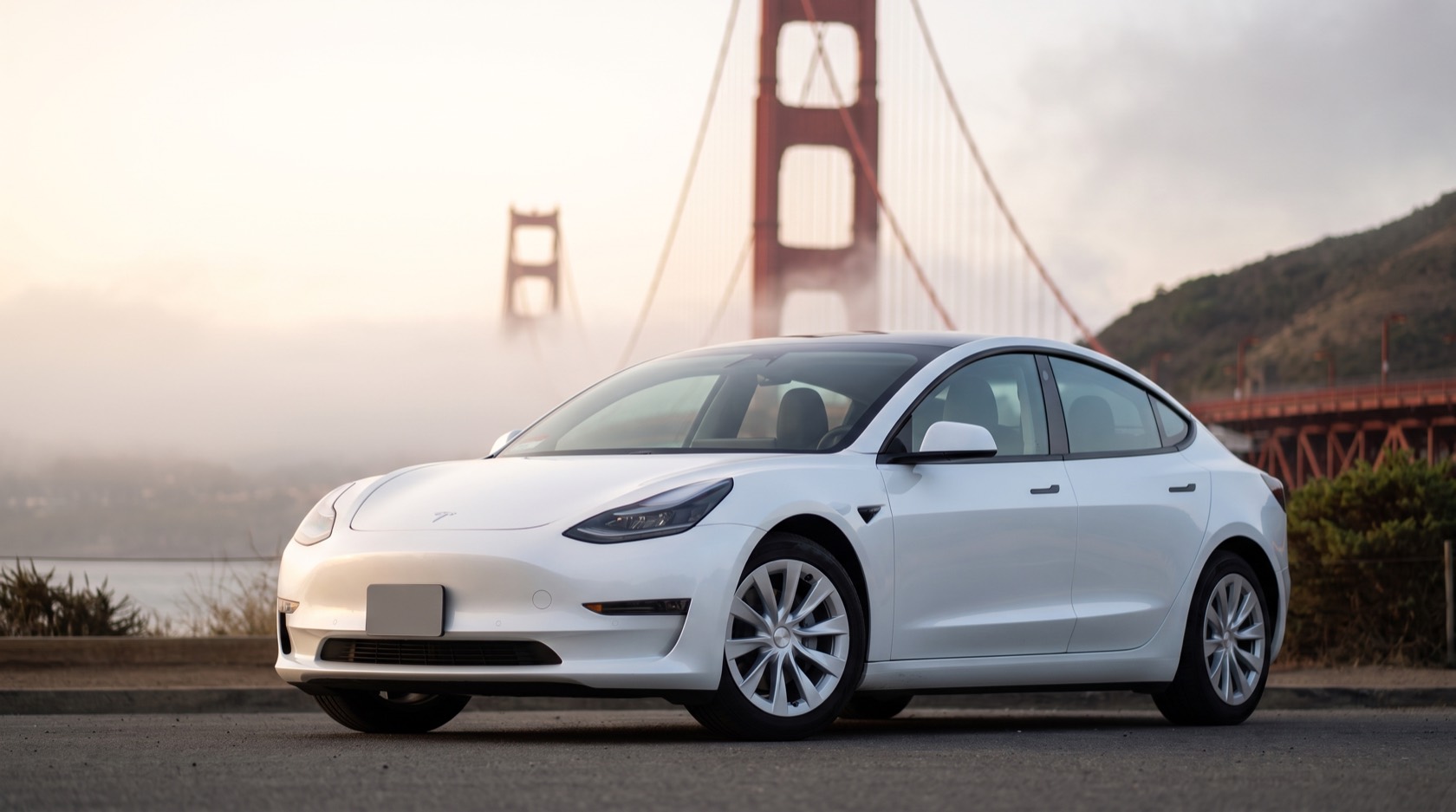 Frost, a white Tesla Model 3, parked below the Golden Gate Bridge rising out of morning fog