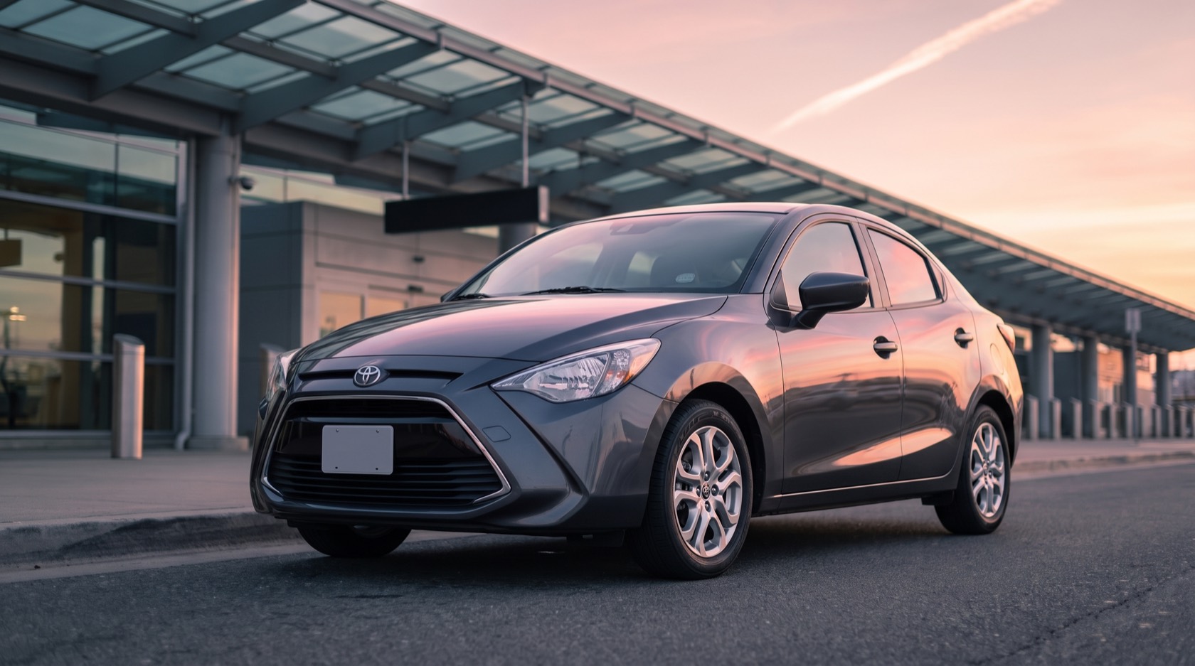 Yaris, a gray 2018 Toyota Yaris iA, at an airport departures curb under a pink dawn sky